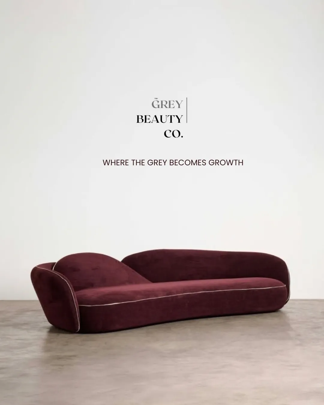 The Grey Beauty Co. brand wall reading Where the Grey becomes Growth, with an oxblood sofa