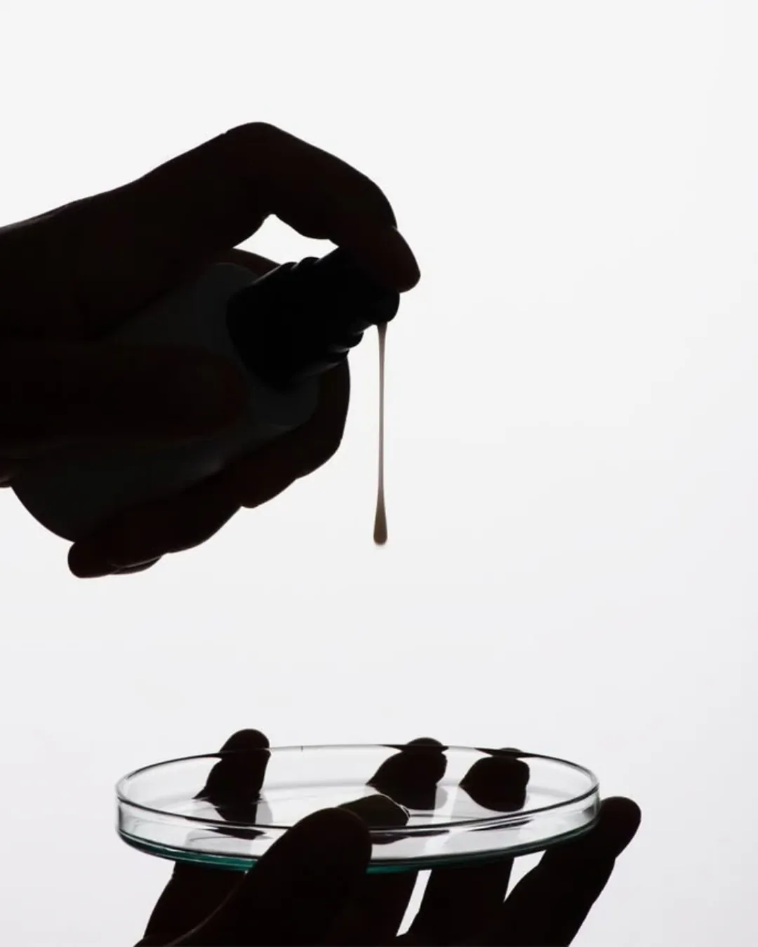 A dropper releasing a drop of serum over a glass dish