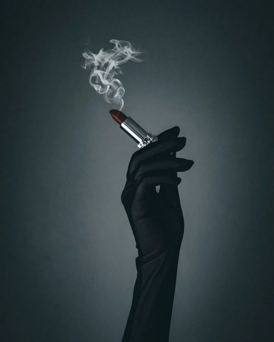 A gloved hand holding a lipstick with smoke rising